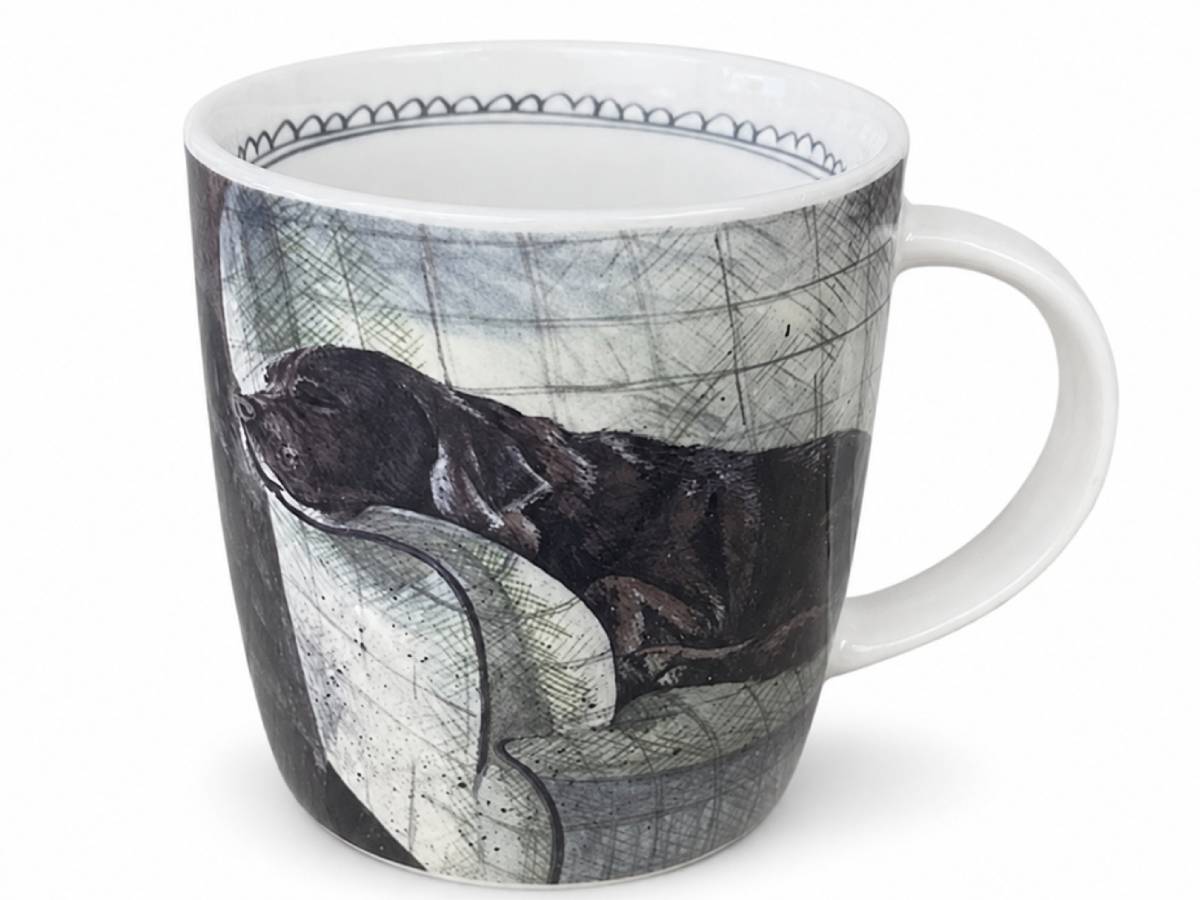 A white ceramic mug featuring a printed illustration of a black dog lying on a gray patterned sofa, shown against a plain white background.