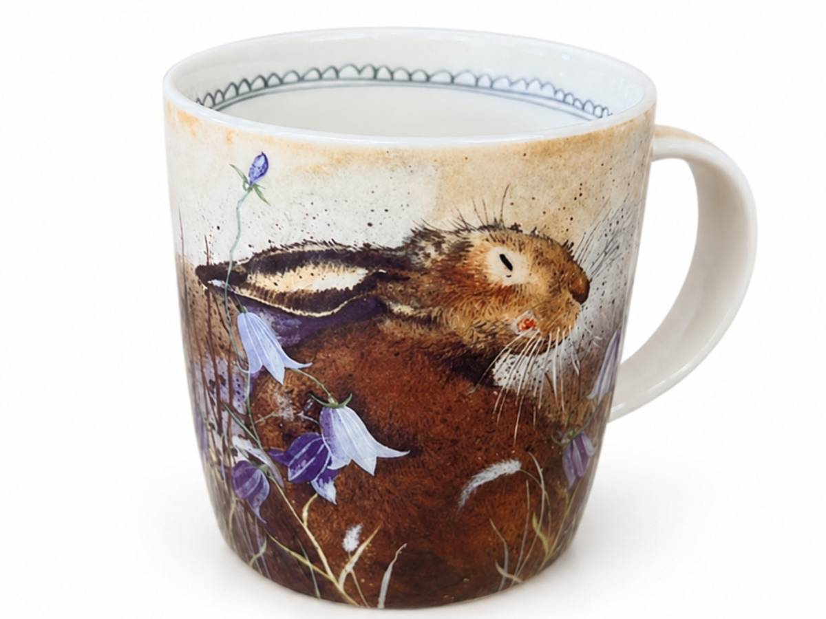 A white ceramic mug featuring a detailed illustration of a brown hare among purple bell-shaped flowers on a light beige background, with a blue patterned rim.