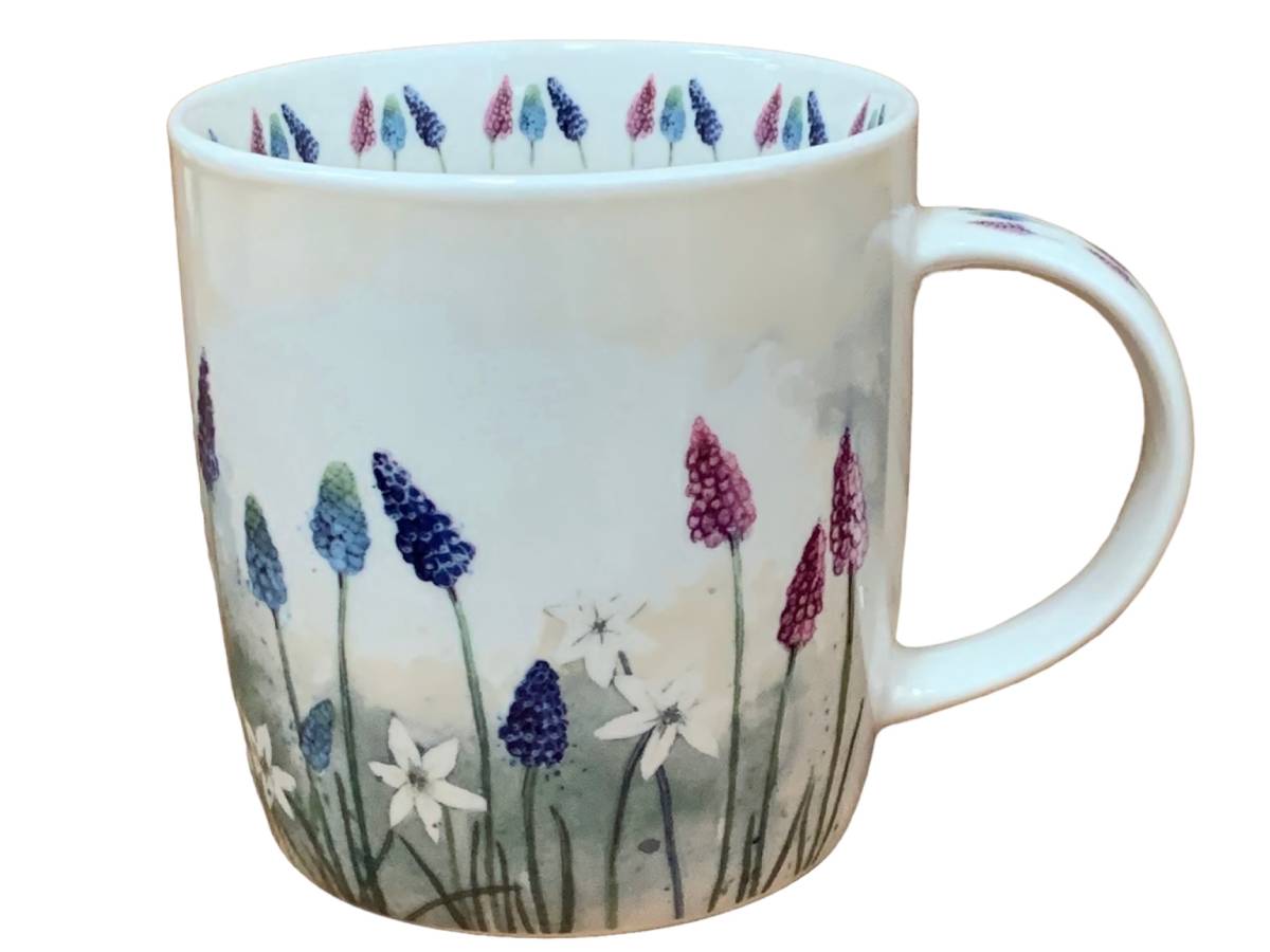 A white ceramic mug decorated with a watercolor-style floral design featuring purple, blue, pink, and white blossoms on a soft light background, with a matching floral pattern around the inner rim.