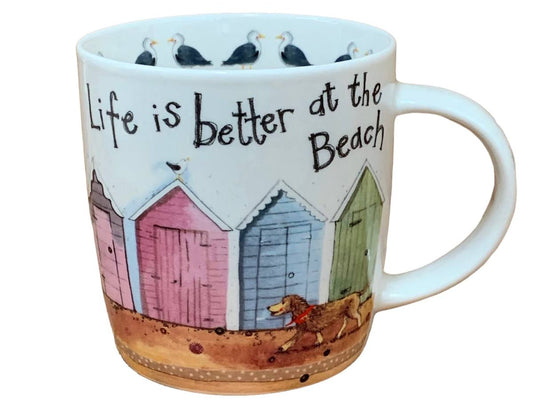 A white ceramic mug featuring a beach-themed illustration with the text 'Life is better at the Beach'. The design includes colorful beach huts in pink, blue, and green, a brown dog, and seagulls along the inner rim, set against a plain white background.