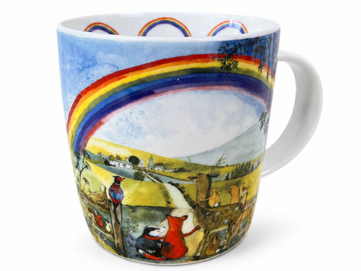 A white ceramic mug featuring a colorful watercolor illustration of a rainbow arching over a pastoral landscape with small animals, shown on a plain white background.