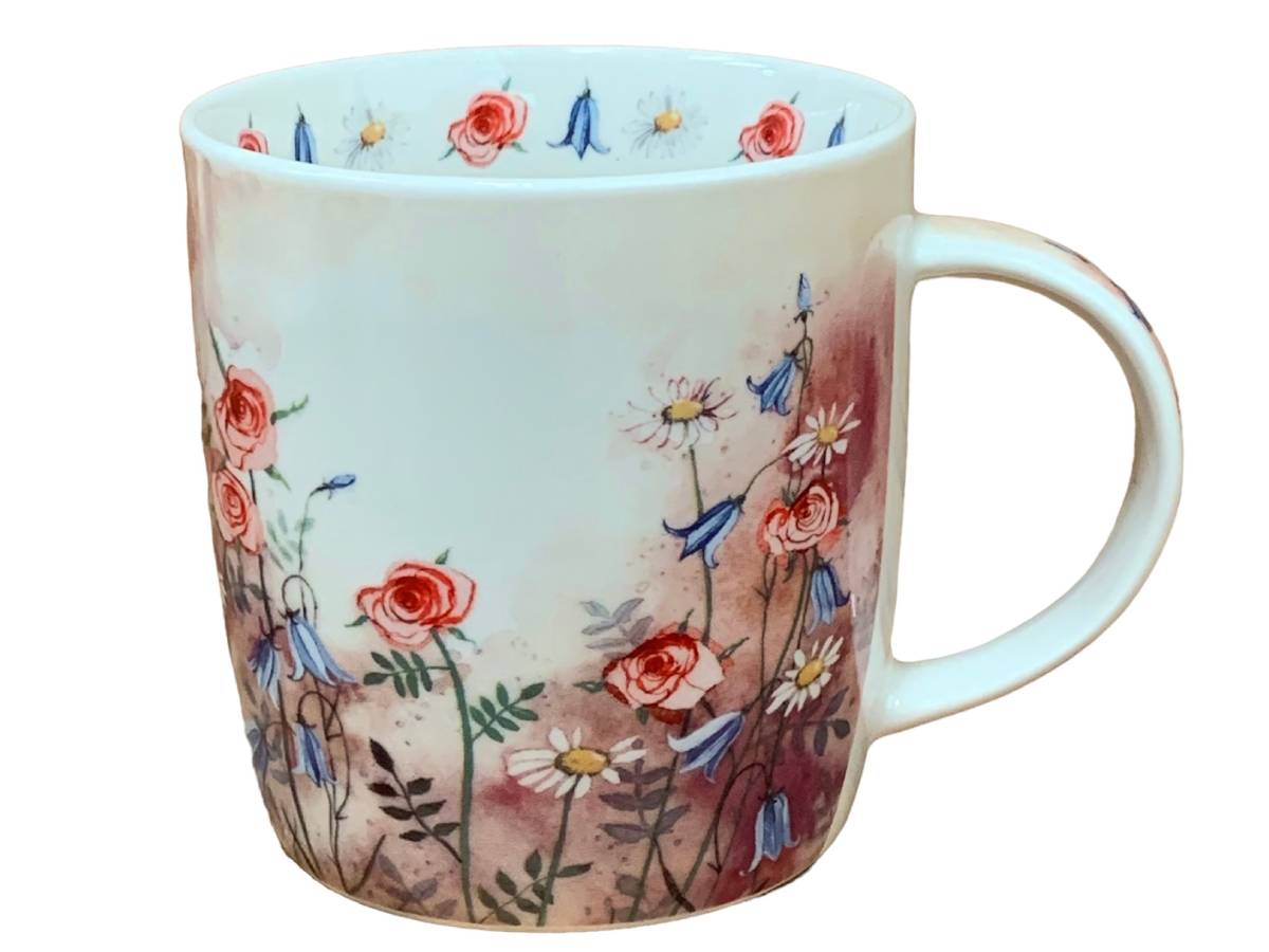 A white ceramic mug decorated with a watercolor-style floral pattern featuring red roses, blue bellflowers, and white daisies on a soft pink and brown background, shown against a plain white background.