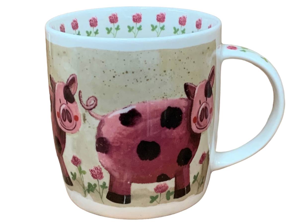 A white ceramic mug featuring a whimsical illustration of pink and black spotted pigs on a speckled beige background, with a pink floral pattern along the inner rim.