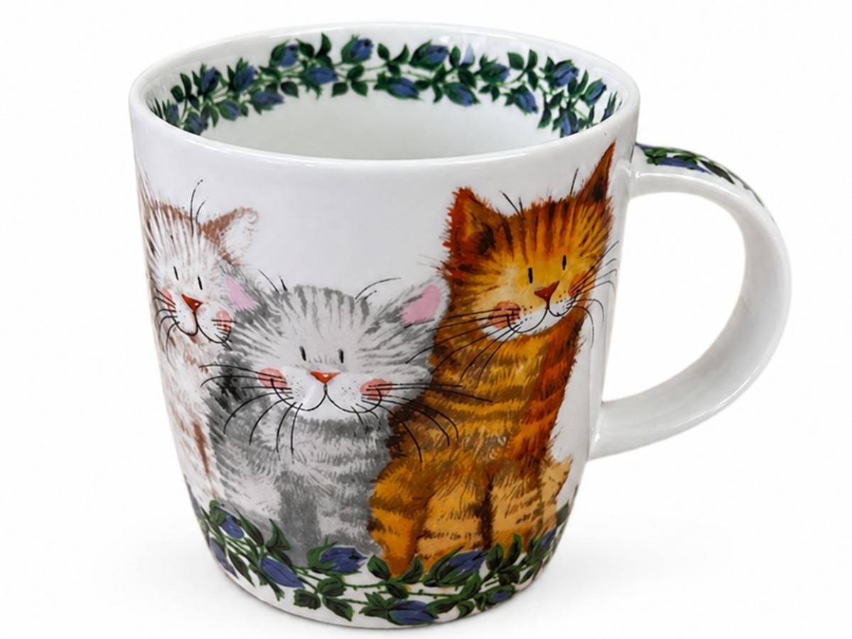 A white ceramic mug decorated with three cute illustrated cats in orange, gray, and cream tones, framed by blue flowers and green leaves at the top and bottom, on a white background.