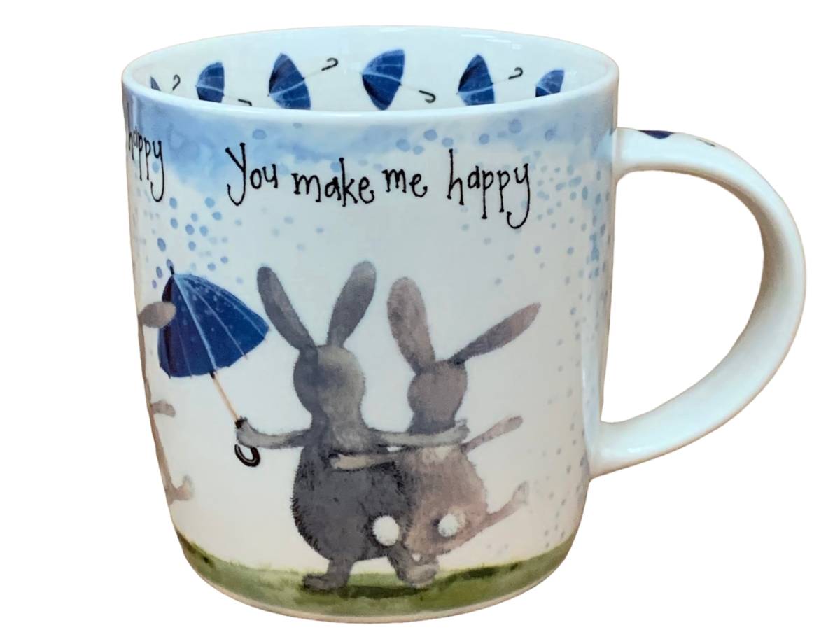 A white ceramic mug featuring a whimsical illustration of two gray rabbits holding blue umbrellas, with the text 'You make me happy' and blue leaf accents on a white background.