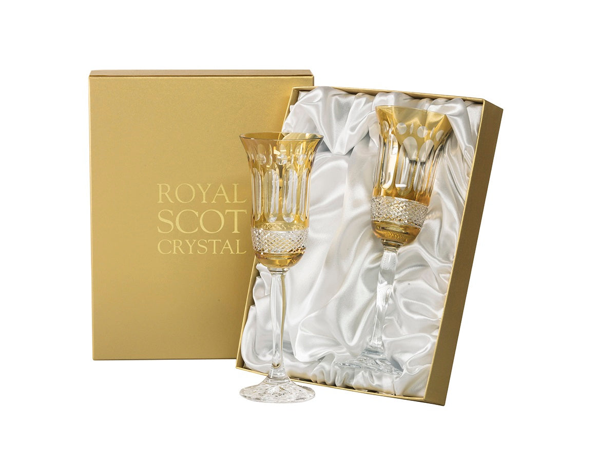 A pair of amber and clear crystal champagne flutes with a relief pattern cut into the outside. They come in a gold presentation box with a white silk lining.