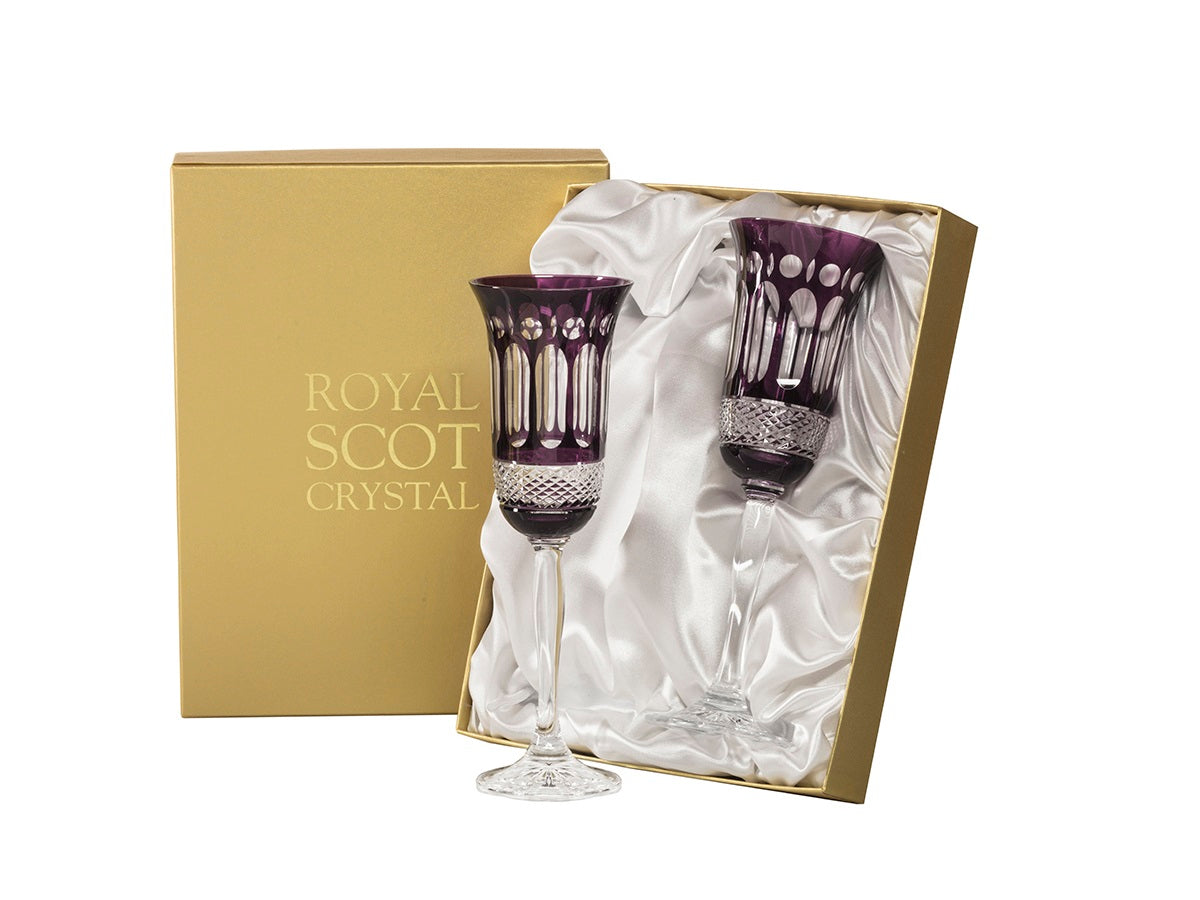 A pair of purple and clear crystal champagne flutes in a gold presentation box with a white silk lining