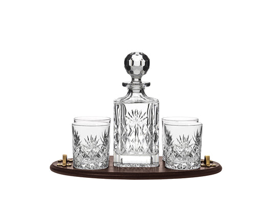 A crystal decanter and four matching tumblers with a cut pattern on the outside, sitting on a solid oak tray with gold handles