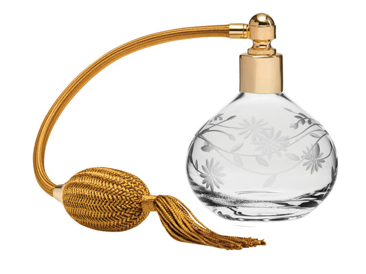 A crystal perfume bottle with a daisy design engraved in the sides, with a gold top and atomiser puffer