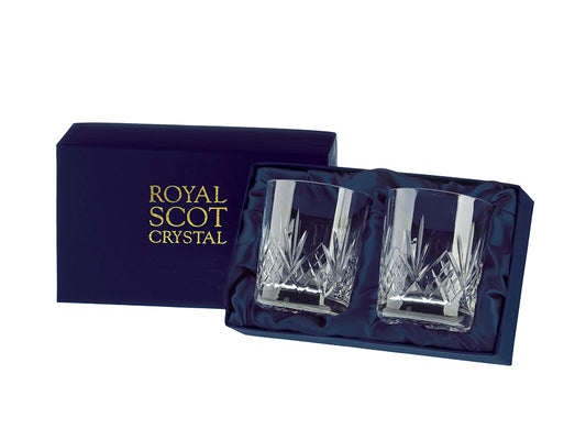 A pair of whisky tumblers with a highland cut, which has a bed of diamonds around the base and a five-pointed fan above them, reaching up towards the smooth rim. They come in a navy-blue silk-lined presentation box with gold branding on the lid.