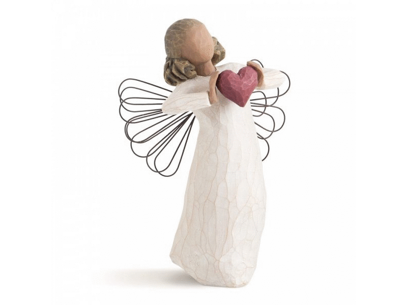 This Willow Tree cast stone figurine portrays a faceless, feminine angel holding out a dark pink 3D heart in her hands. She wears a white dress, and her wire wings, resembling sparkler art, adorn her back. Painted in soft, earthy tones of cream, beige, and brown.