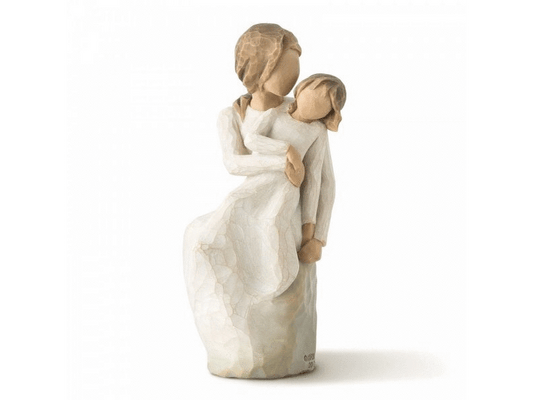 A cast stone duo figurine features a faceless mother holding a faceless daughter on her lap in a warm embrace. The earthy soft colors and lack of features allow for personal interpretation.