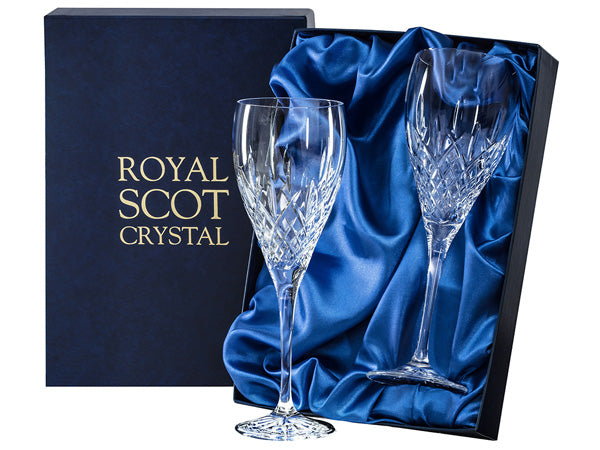 A pair of crystal wine glasses with a London cut design around the outside of the bowl, which has a bed of diamonds around the base and single flicks going up towards the smooth rim. They come in a navy-blue silk-lined presentation box with gold branding on the lid.
