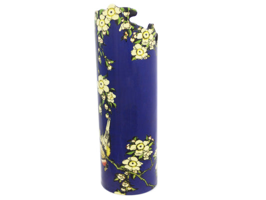 A slender porcelain vase that is part of John Beswick's Silhouette D'Art collection. It has a navy blue base and depicts a robin perched among blooming yellow flowers, and the tip edge of the vase is moulder to mimic the curvature of the flower petals.