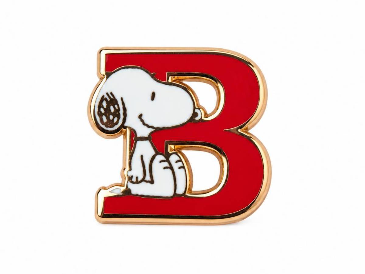 A Snoopy enamel pin shaped like a large red letter B with gold-tone metal outlines. Snoopy is depicted sitting inside the letter, in white with black details.
