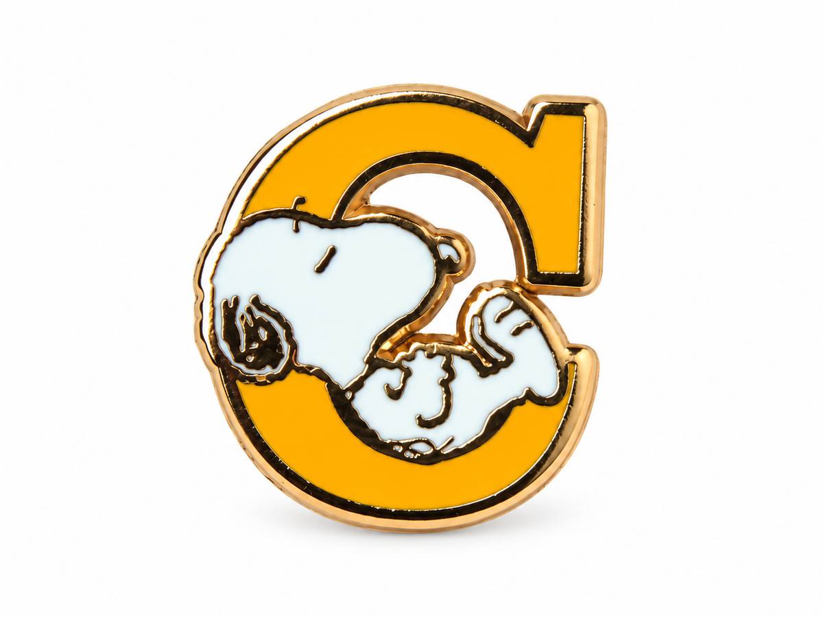 A gold-plated enamel pin shaped like the letter 'C', featuring Snoopy and Woodstock in white with black outlines, set against a plain white background.