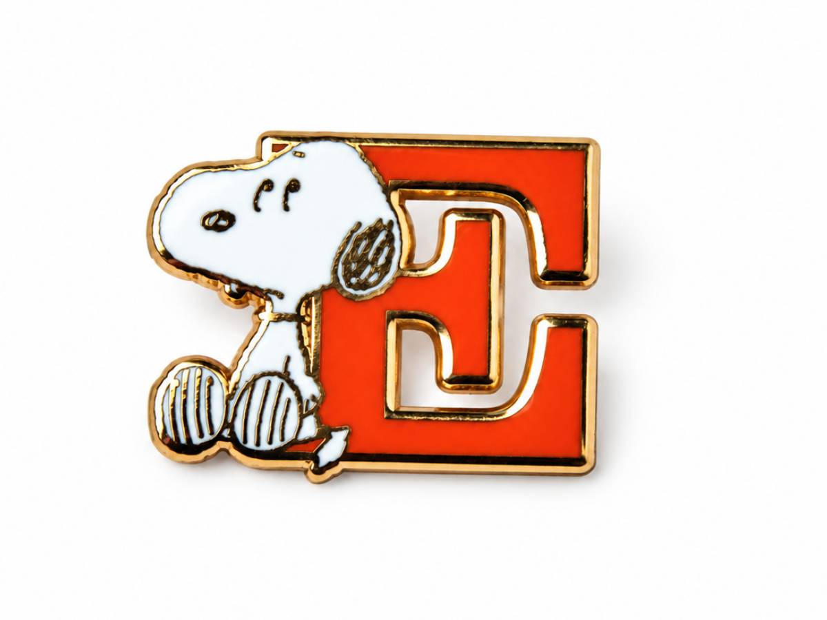 A Snoopy enamel pin featuring the character sitting on a large red letter 'E' with gold-tone metal outlines, shown on a plain white background.