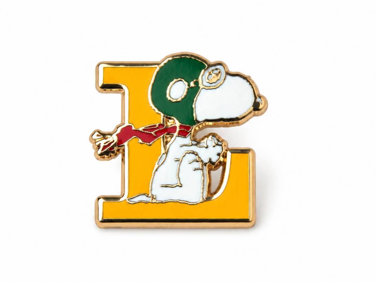 A Snoopy enamel pin featuring the letter 'E' in gold with Snoopy wearing a green Santa hat and red scarf, set against a plain white background.