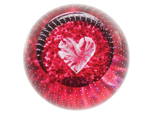 A glass paperweight in a rich pink red colour, with a kaleidoscopic effect around a white heart in the centre of the paperweight