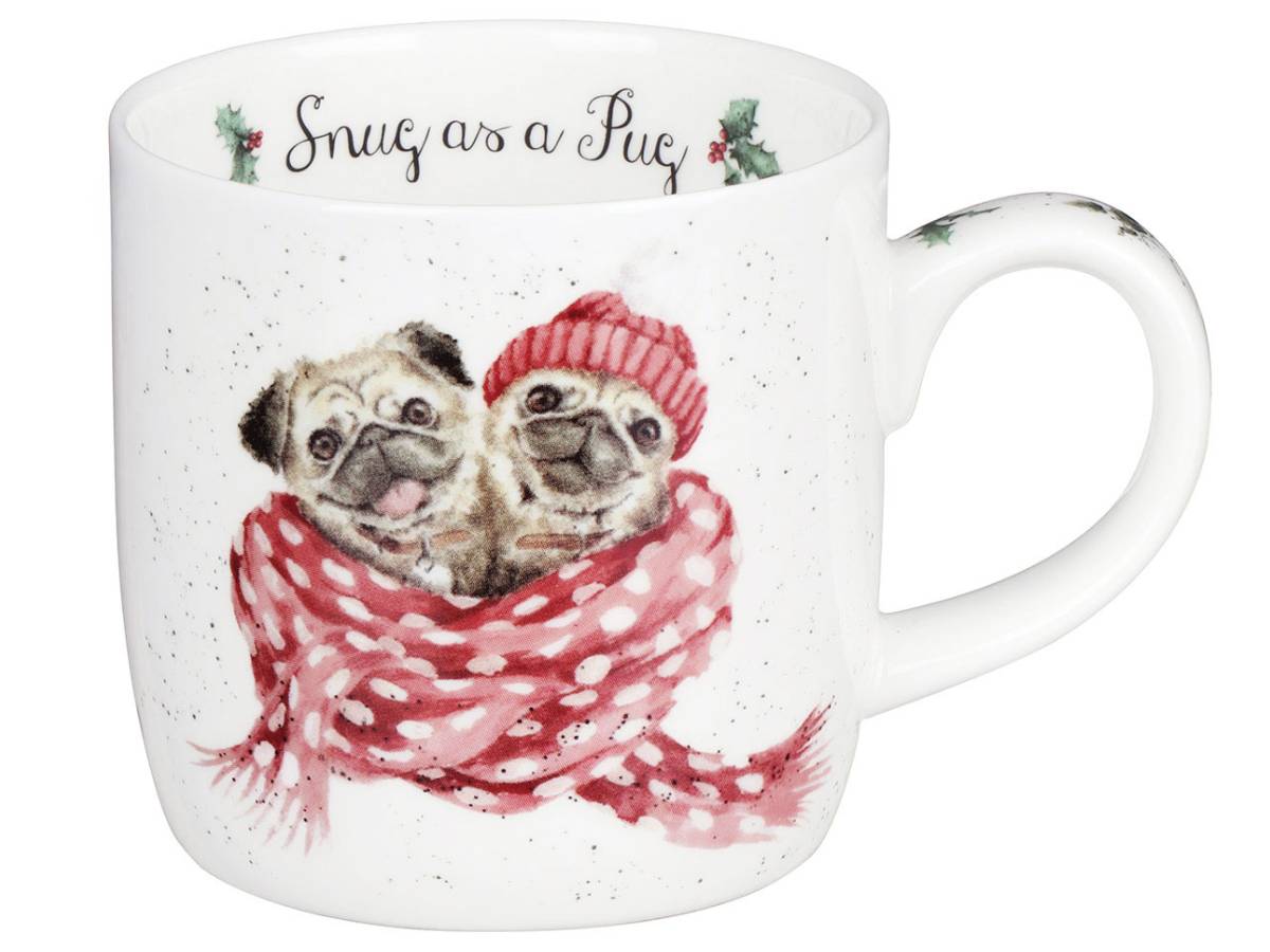 A white ceramic mug featuring a watercolor illustration of two pug dogs wrapped in a red and white polka-dot scarf and matching red knit hat. The top rim of the mug has the phrase 'Snug as a Pug' written in black script with small holly accents.