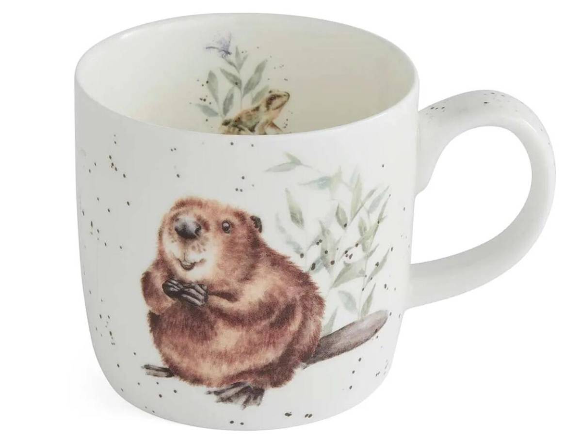 A white ceramic mug featuring a detailed illustration of a brown beaver surrounded by green leaves and small black speckles, with a frog and butterfly motif visible inside the mug.