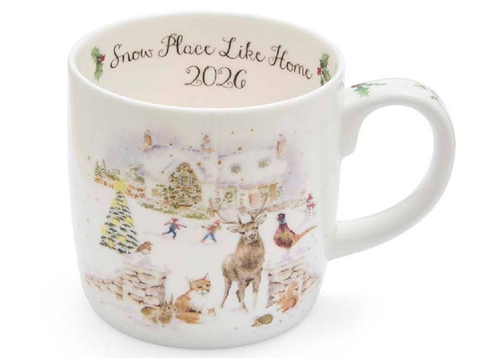 A white ceramic mug featuring a winter village illustration with a deer, dog, hen, and small houses, with the text 'Snow Place Like Home 2026' printed inside the mug.